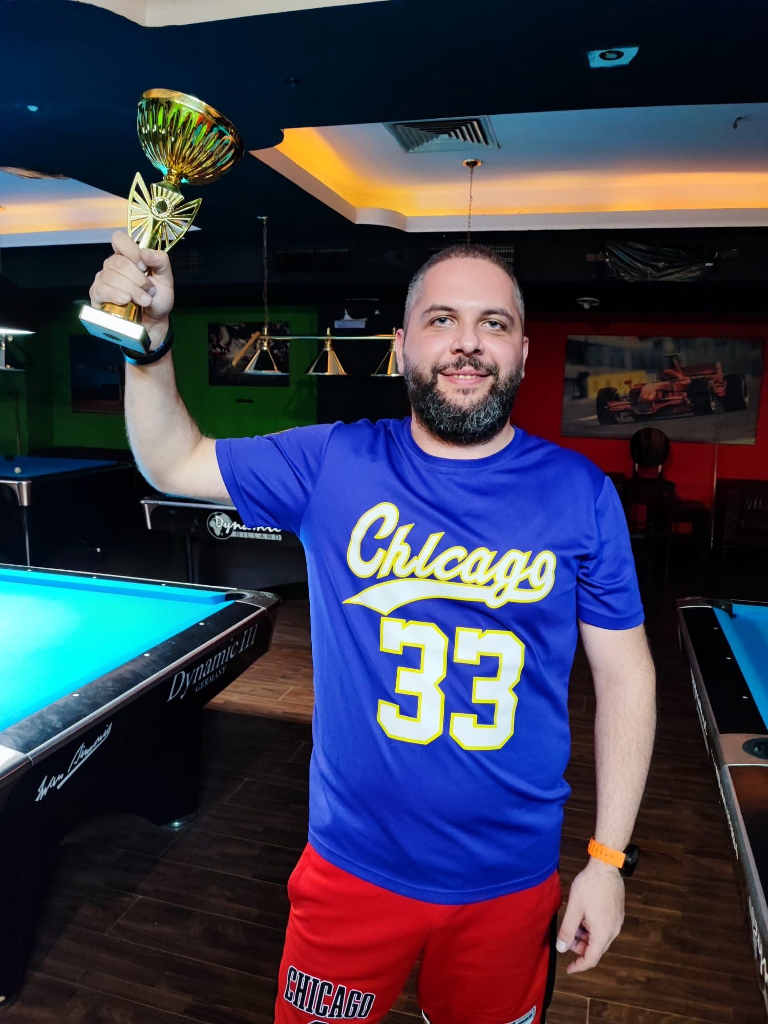 Horia Teodorescu ridicând trofeul câștigat, lângă o masă de biliard